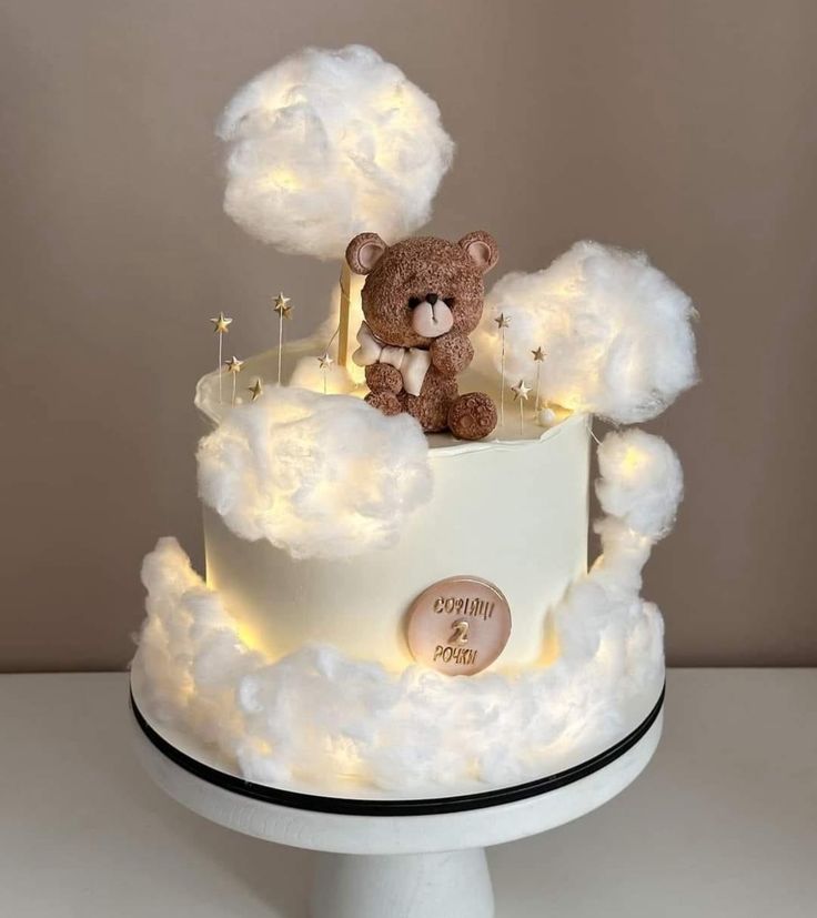 a teddy bear sitting on top of a cloud covered cake with lights in the shape of clouds