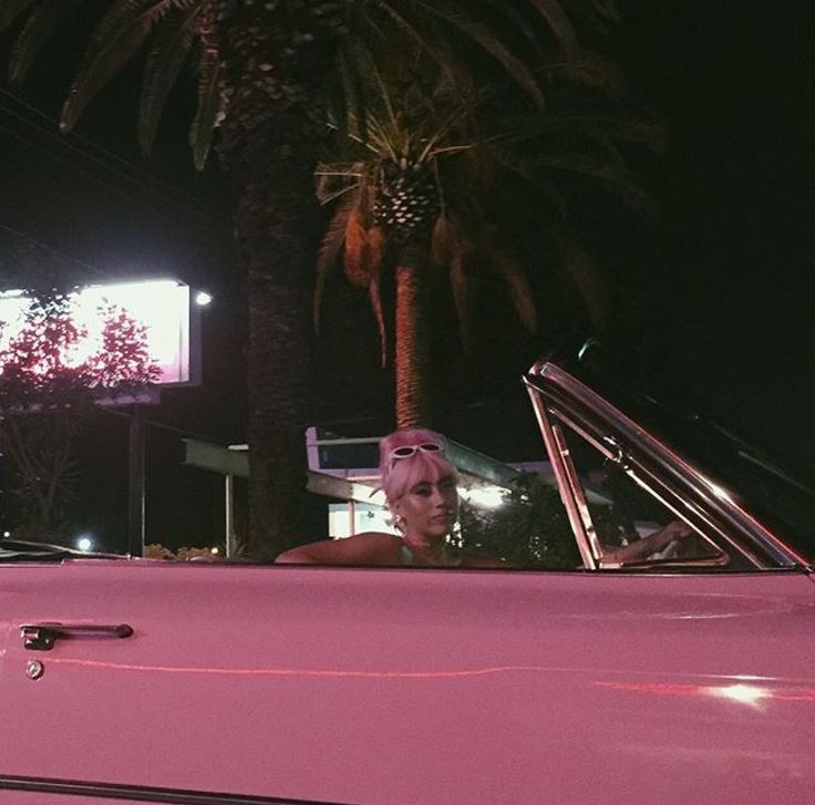 a woman sitting in the driver's seat of a pink convertible car at night