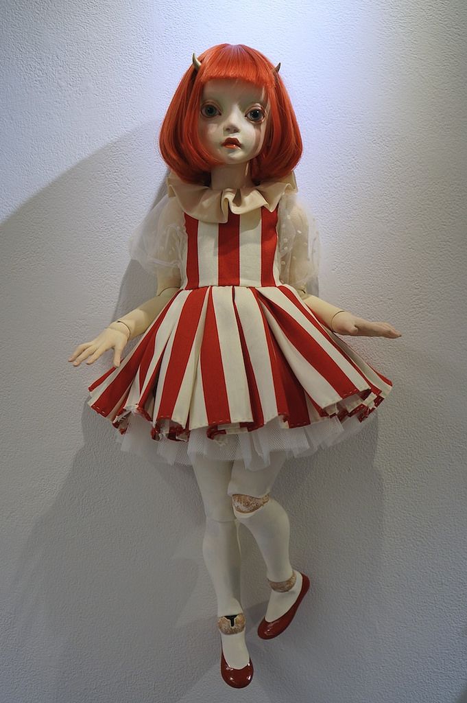 a doll dressed in red and white striped dress with horns on her head, standing next to a wall