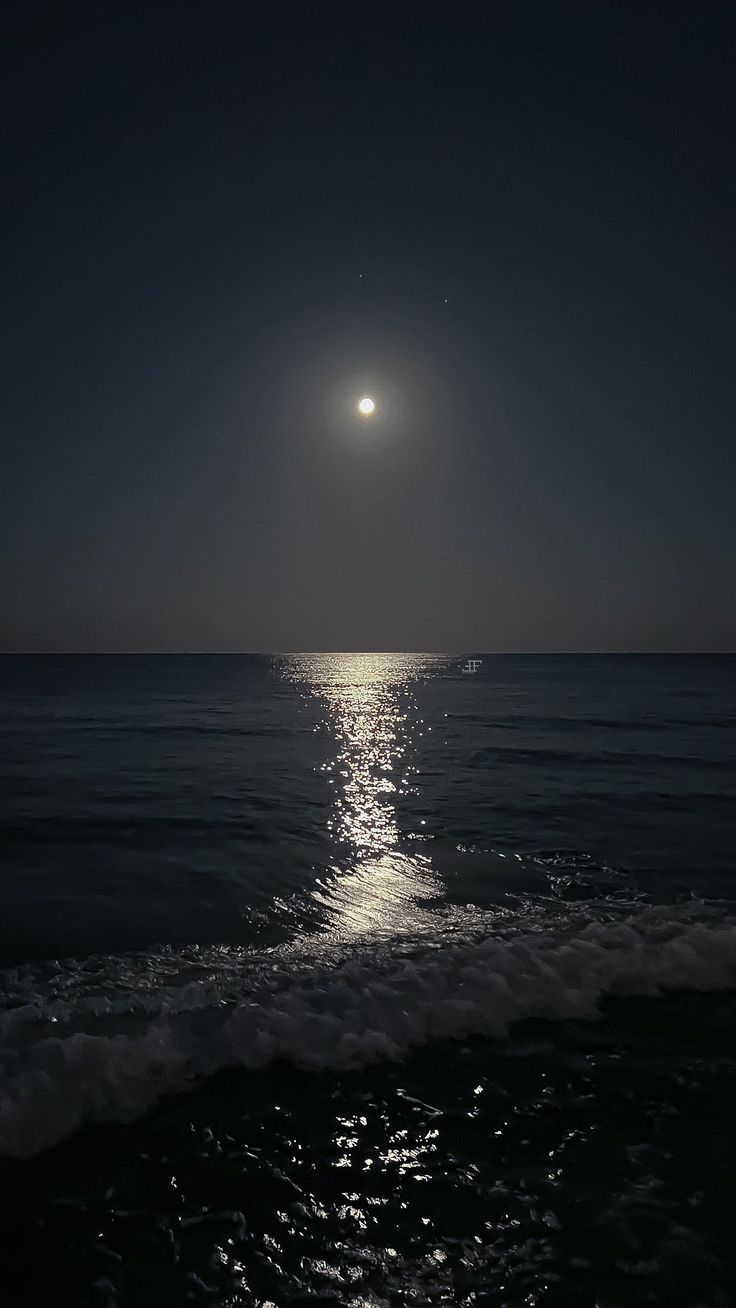 the moon is shining over the ocean at night