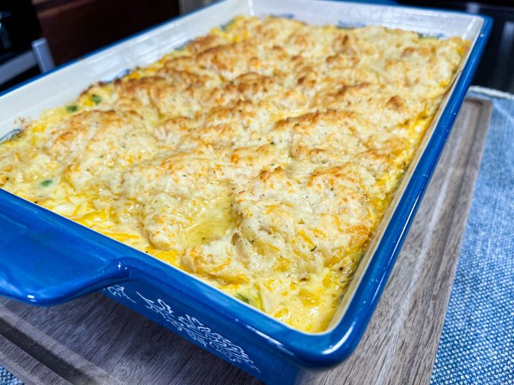 a blue casserole dish with cheese on top sitting on a wooden table next to a glass container