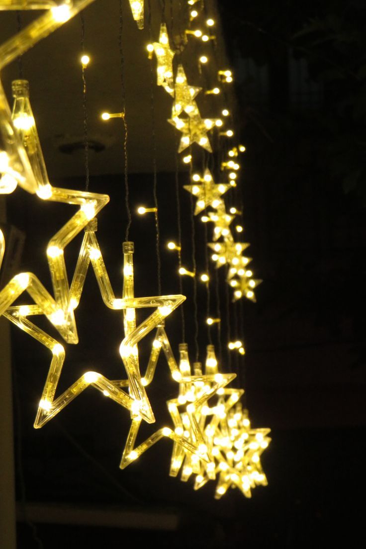 lighted stars hanging from the ceiling in front of a building with lights all around them