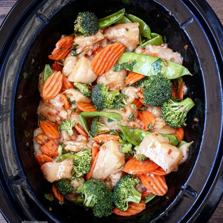 a black bowl filled with vegetables and meat on top of a wooden table next to utensils