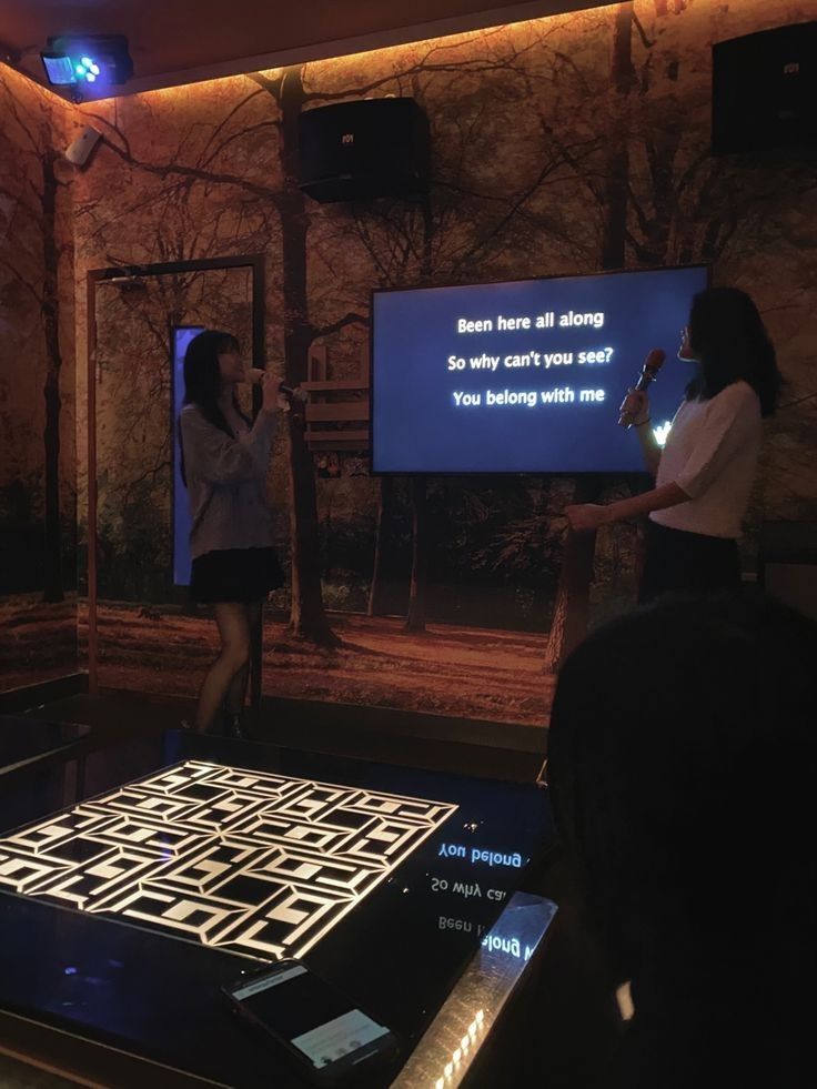 two women are standing in front of a screen with a video on it and one is holding a microphone