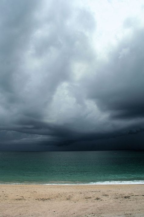 an empty beach under a cloudy sky with the ocean in the background