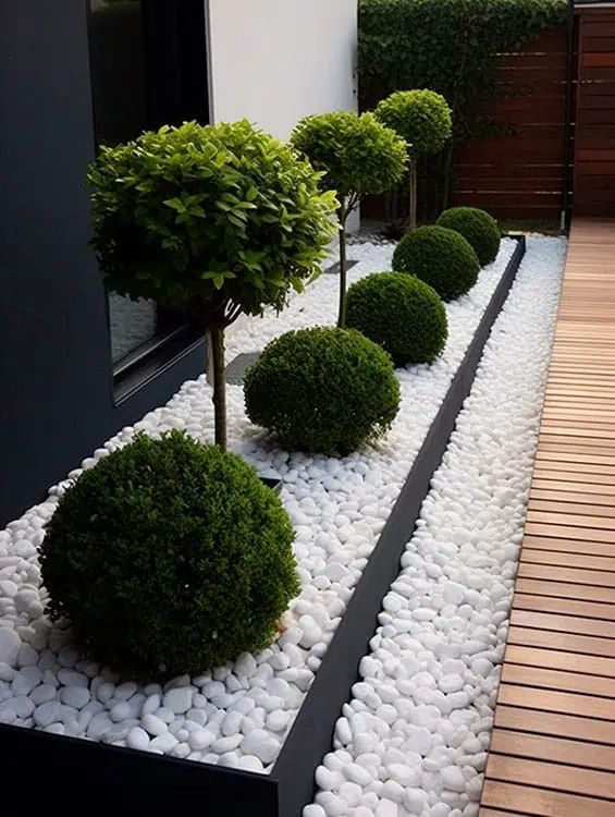 a garden with white rocks and trees in the center, along side a building that has a wooden deck