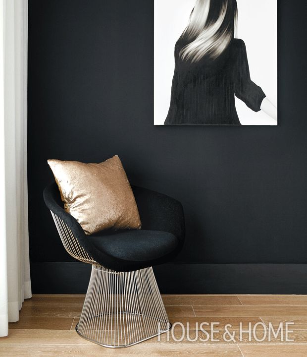 a black chair in front of a painting on the wall and a gold pillow sitting next to it