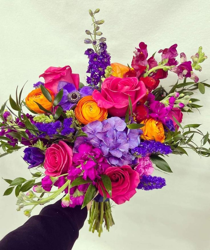 a person holding a bouquet of colorful flowers in their left hand, on a white background