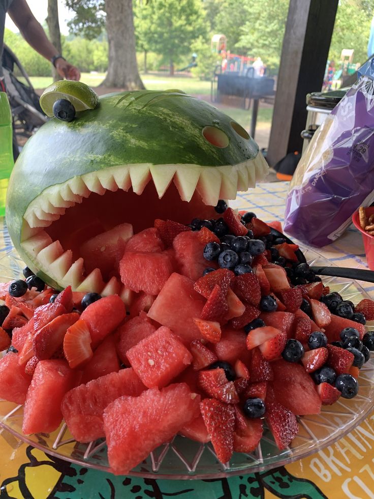 a watermelon shark with its mouth open and fruit salad in the foreground