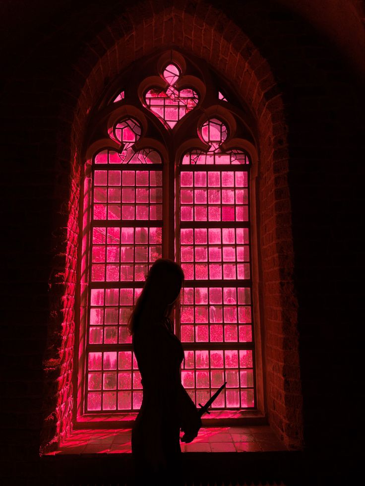 a woman standing in front of a window with red light coming from it's windows