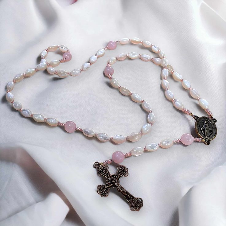 This special rosary is a lighter version of our signature Parable of Pearls Rosary. Perfect for a young girl - perhaps a Baptism or first Holy Communion. It features rice-shaped mother of pearl beads for the decades and rose quartz for the Our Fathers, as well as Czech glass shiny pink spacers, and a bronze Miraculous Medal and crucifix made in Italy. Spiritual Pearl Rosary As Gift, Mother's Day Spiritual Rosary, Pearl Rosary For First Communion, Spiritual Style, Spiritual Pearl Rosary For First Communion, Pearl White Spiritual Rosary As Gift, Spiritual Pearl White Rosary Gift, Spiritual Pearl White Rosary As Gift, St Michael Medal, Handmade Tapestries