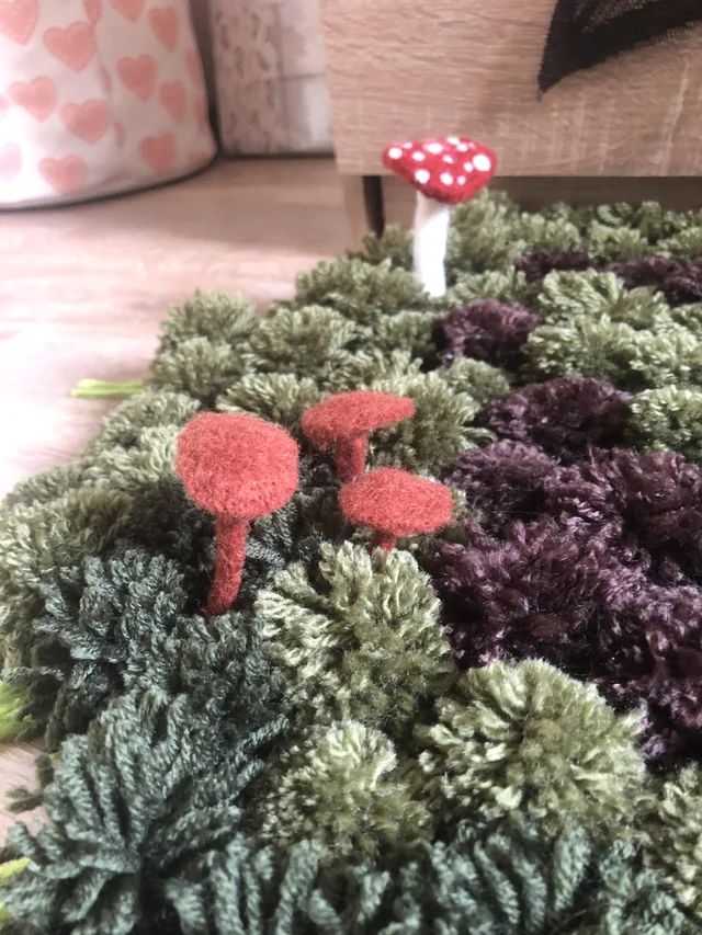 two red mushrooms sitting on top of some green mossy plants in front of a couch