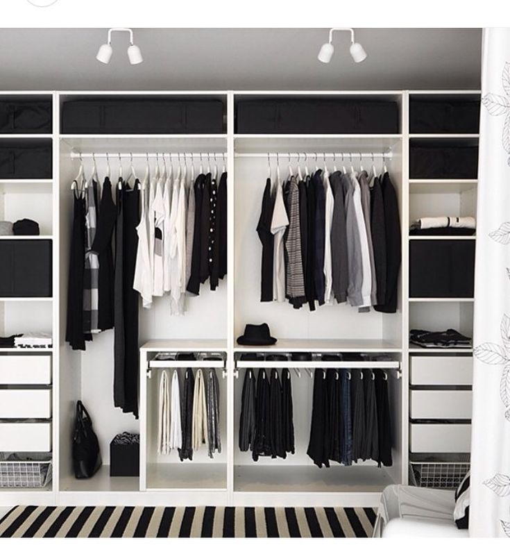 a white closet with black and white clothes hanging on the walls, drawers, and shelves