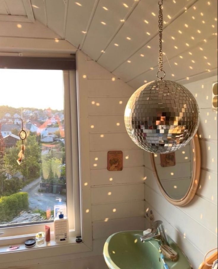 a disco ball hanging from the ceiling above a sink in a bathroom with a window