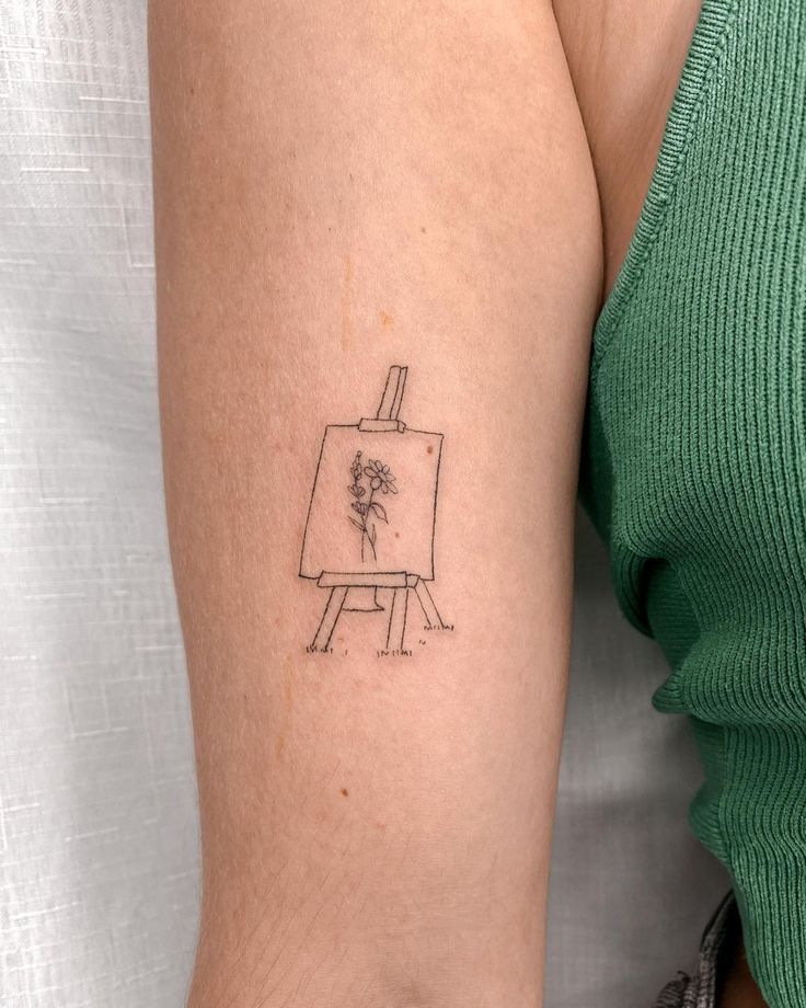 a woman's arm with a drawing easel tattoo on her left upper arm