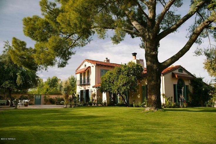 a large house sitting on top of a lush green field next to a tall tree