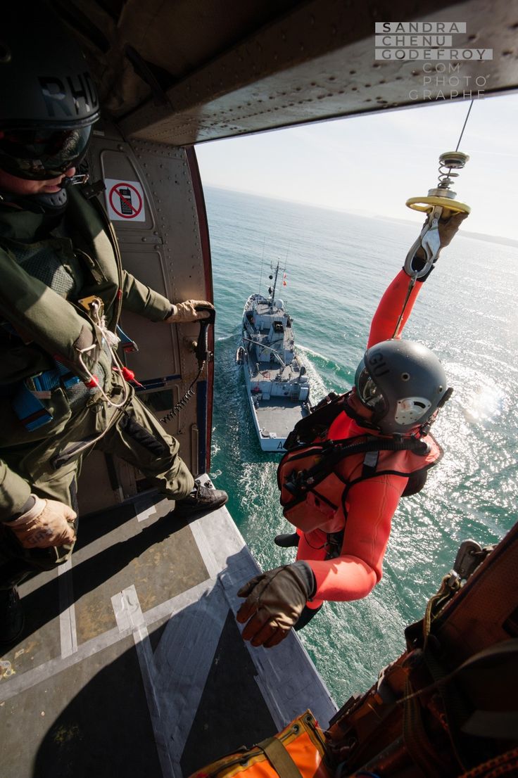 a man in an orange life jacket is hanging off the side of a helicopter with another person on it