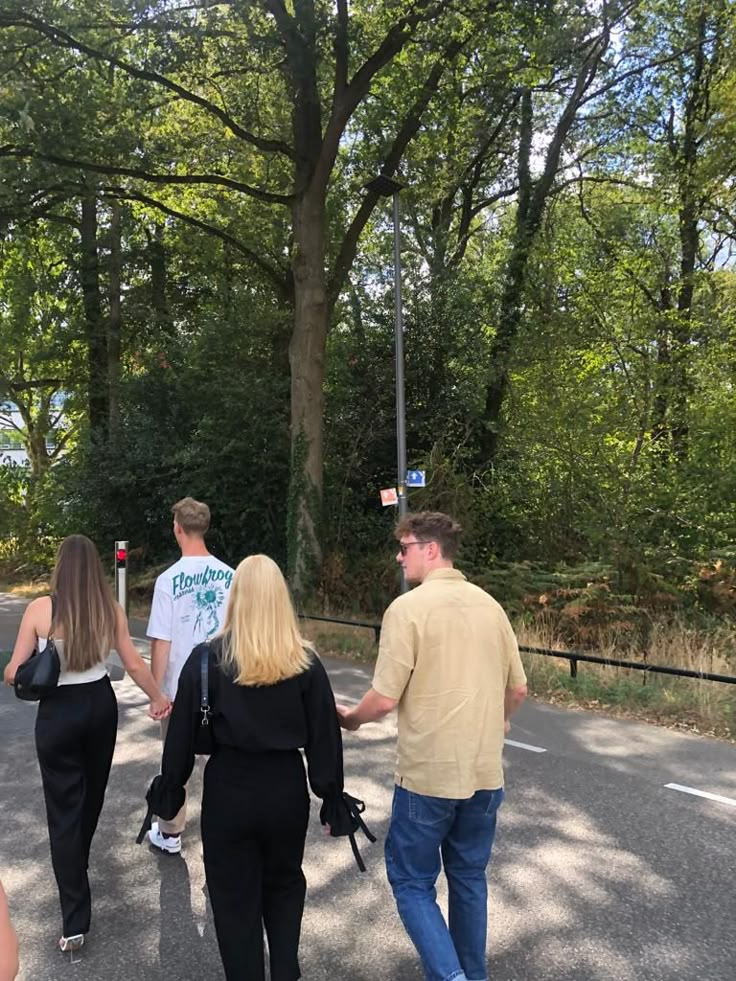 three people walking down the street holding hands and talking to each other with trees in the background