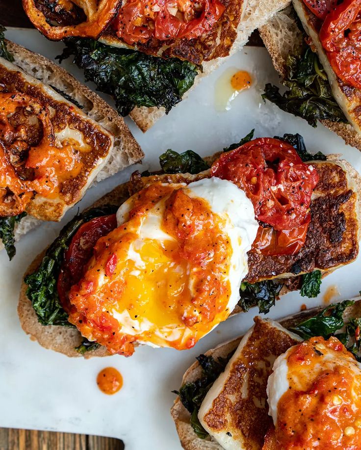 several open faced sandwiches topped with eggs and spinach on top of a white plate