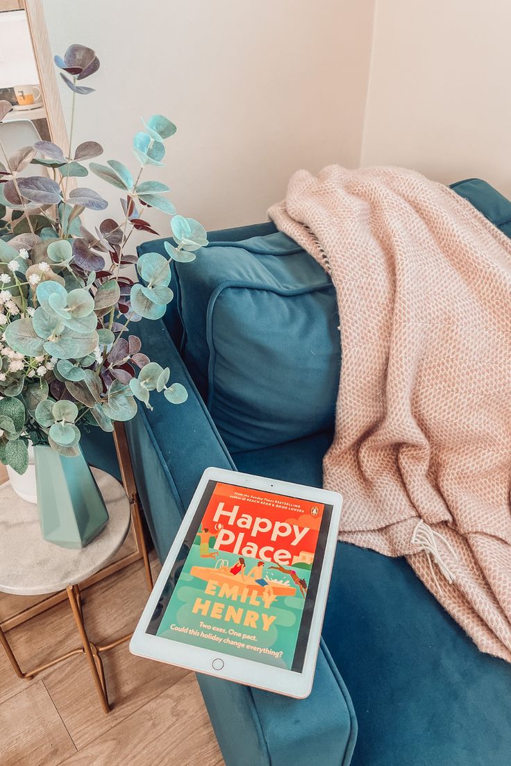 a tablet sitting on a blue couch next to a vase with flowers and a pink blanket