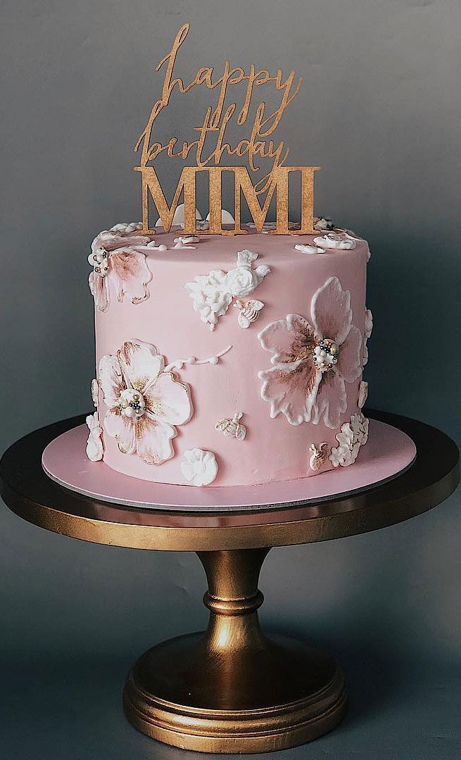 a pink cake with gold lettering and flowers on the top is sitting on a pedestal