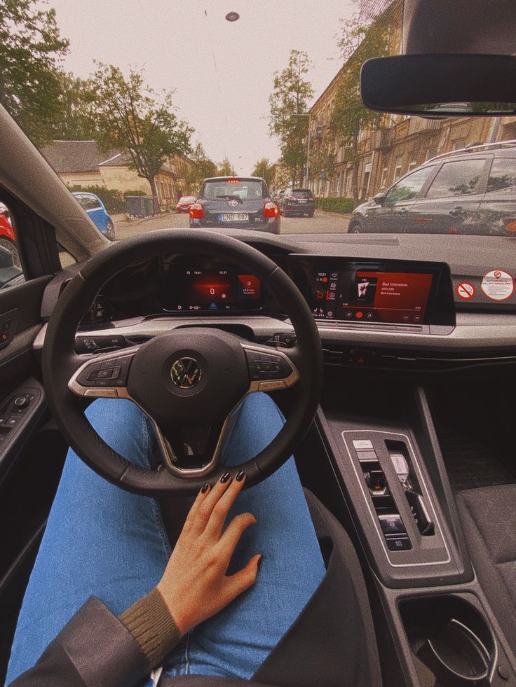 a person sitting in the driver's seat of a car with their hand on the steering wheel