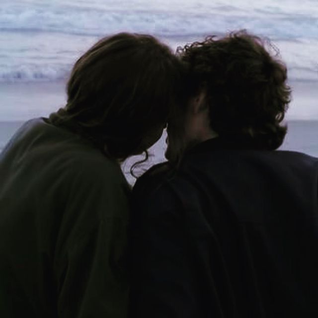 two people standing next to each other near the ocean