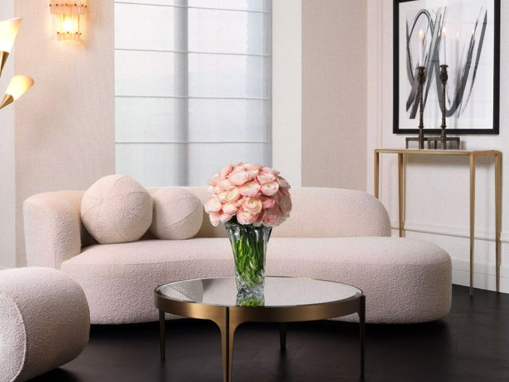 a living room with white couches and pink flowers in a vase on the coffee table