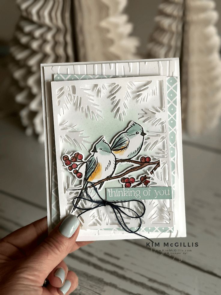 a hand holding up a card with a bird on it and berries in the background