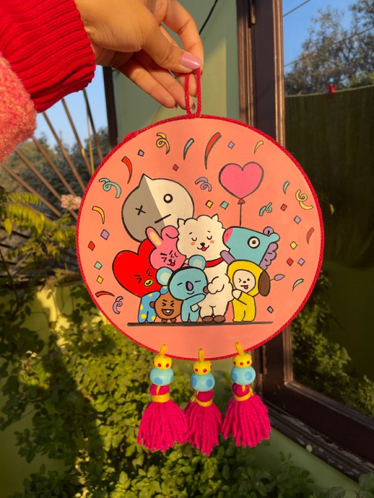 a person holding up a pink paper plate with cartoon characters on it and tassels