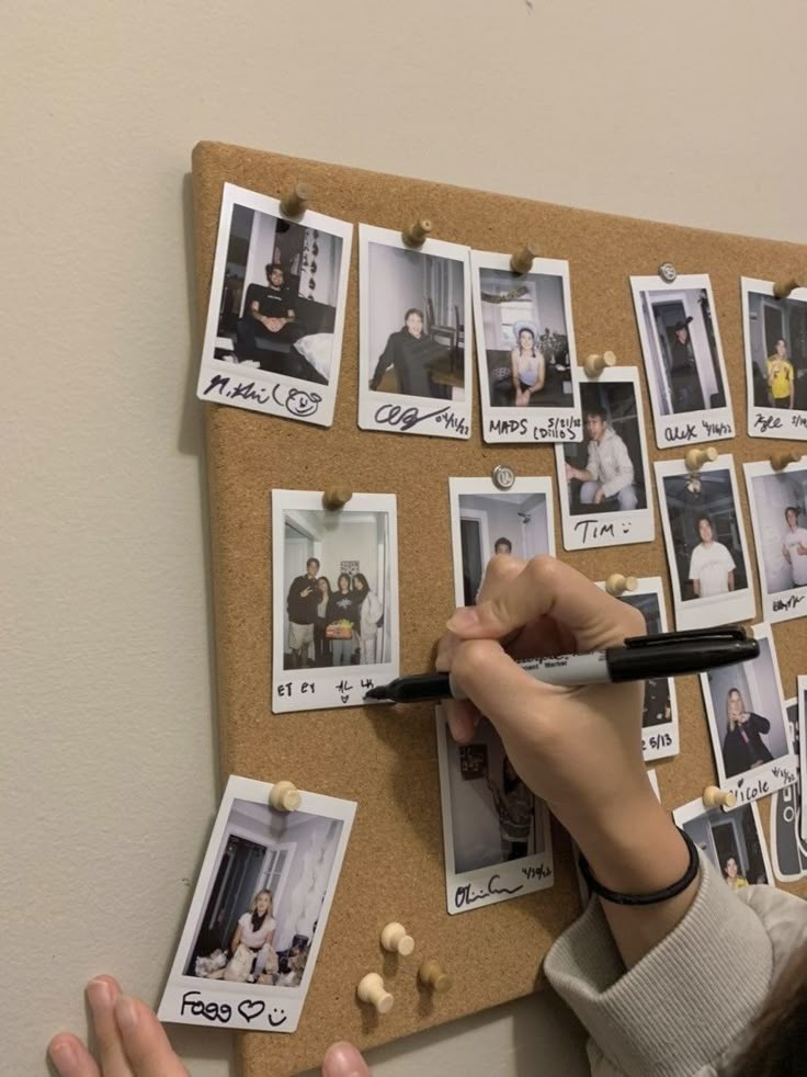 a woman is holding a pen and writing on a cork board with photos pinned to it