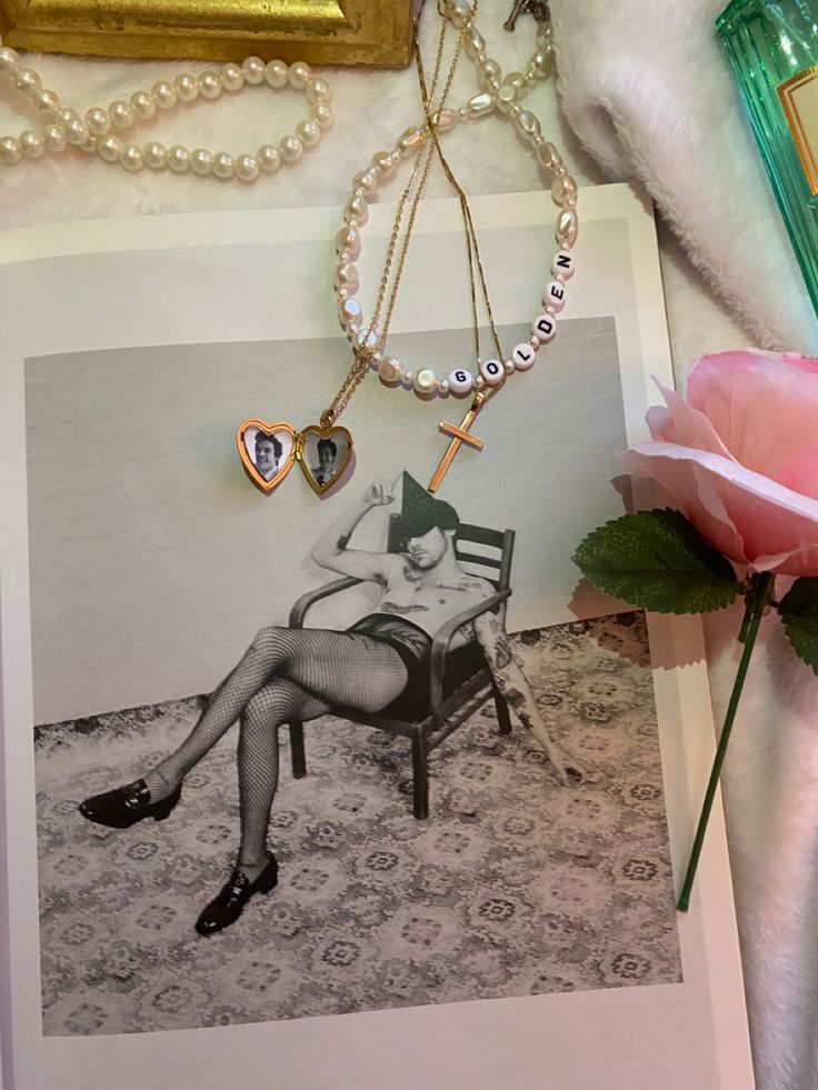 a pink rose sitting on top of a table next to an old photo and necklace