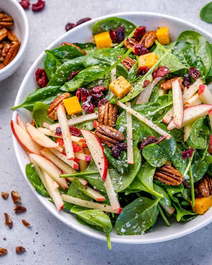 a salad with apples, cranberries and pecans in a white bowl on a table