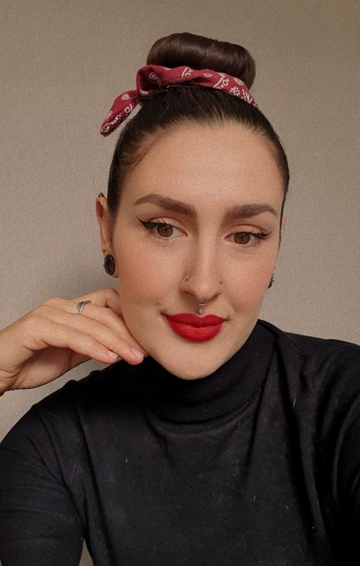 a woman with a red bow in her hair wearing a black turtle neck top and matching earrings