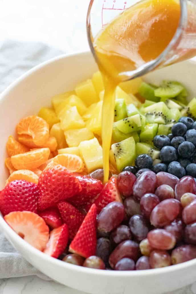 someone pouring orange juice into a white bowl filled with fresh berries and kiwis