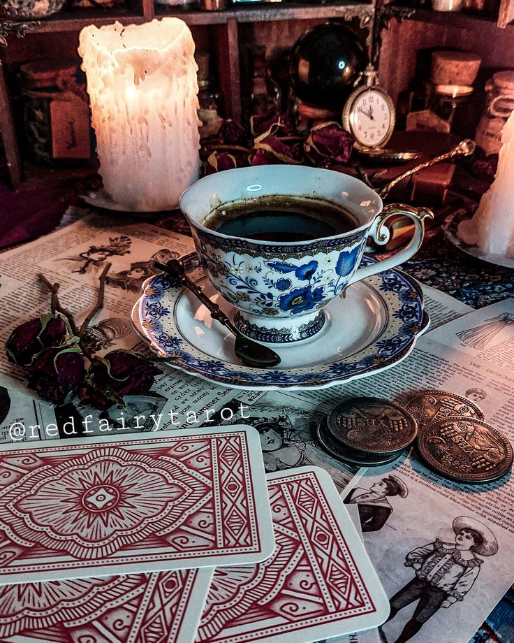 a cup of coffee sitting on top of a table next to some cards and candles