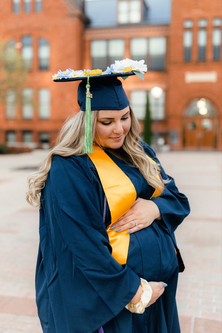 a woman wearing a graduation gown and holding her baby