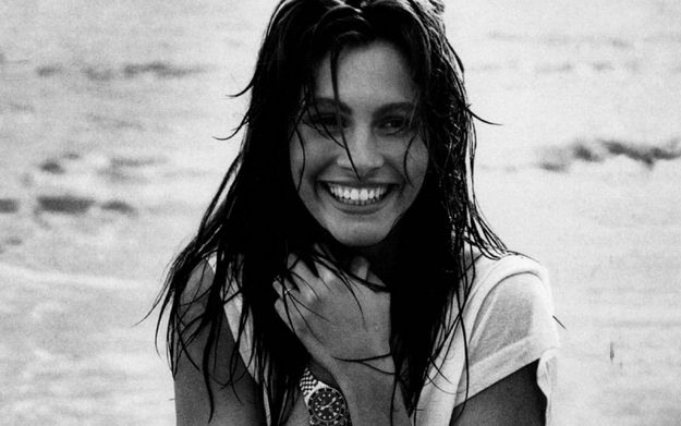 a woman standing on top of a beach next to the ocean with her hands in her pockets