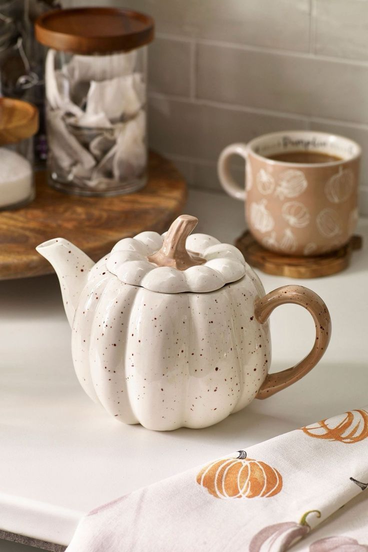 a white ceramic tea pot sitting on top of a counter next to a coffee cup