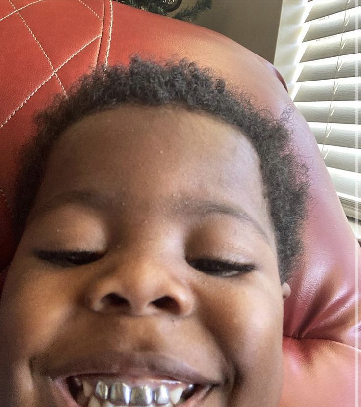 a young child smiling while sitting on a red leather chair in front of a window