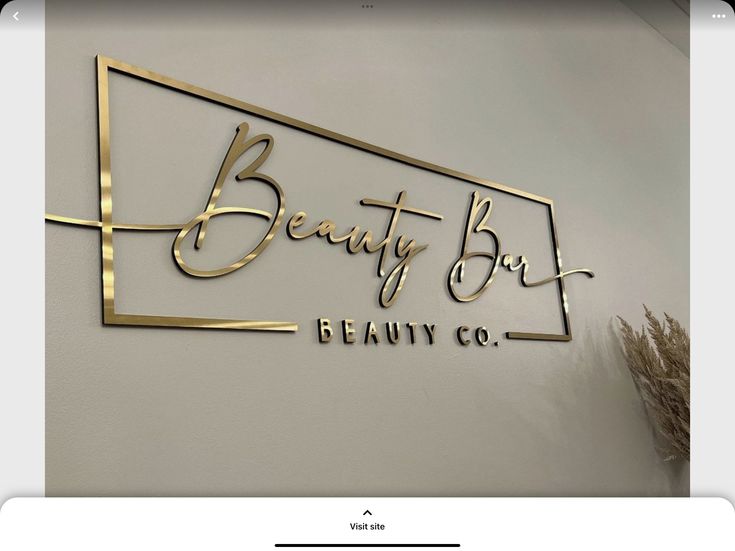 the beauty box logo is gold and black on a white wall with a plant next to it