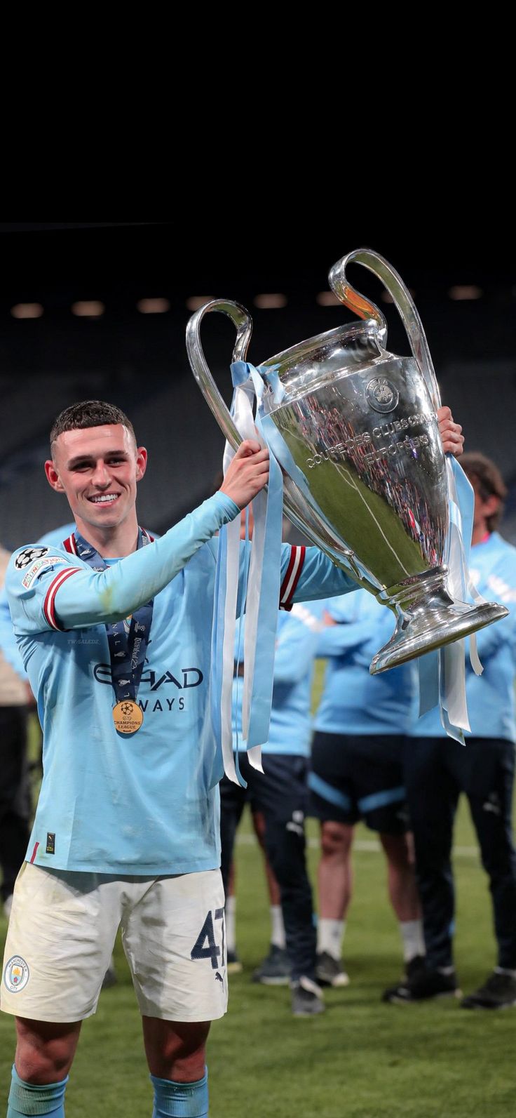 a man holding up a silver trophy on top of a soccer field with other people behind him