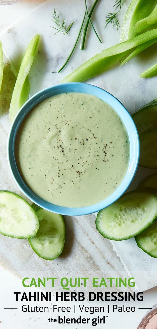 a blue bowl filled with green liquid surrounded by sliced cucumbers on a white surface