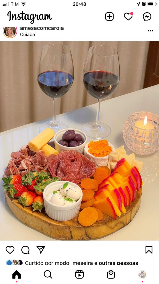 two glasses of wine sit on a table with cheese, meat and fruit in front of them