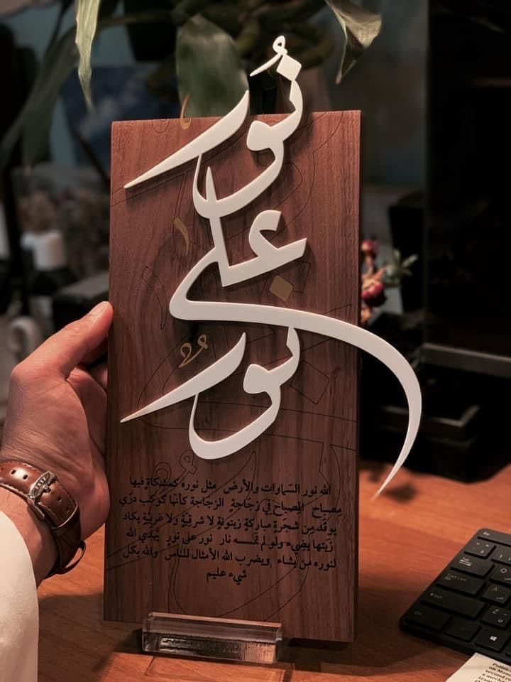 a person holding up a wooden plaque with arabic writing on it, in front of a computer keyboard