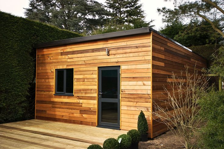 a small wooden building sitting on top of a wooden deck next to a green hedge