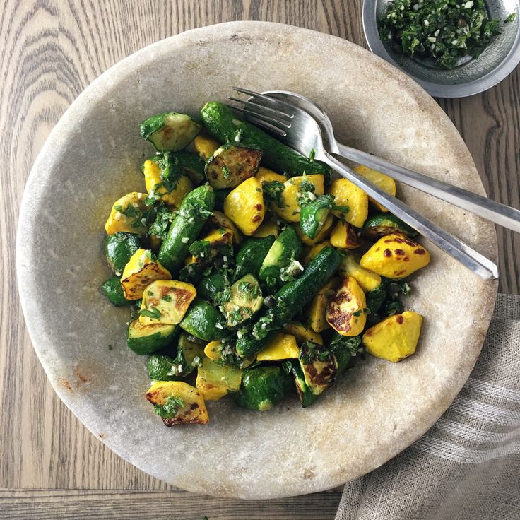 a white bowl filled with vegetables on top of a wooden table next to a fork