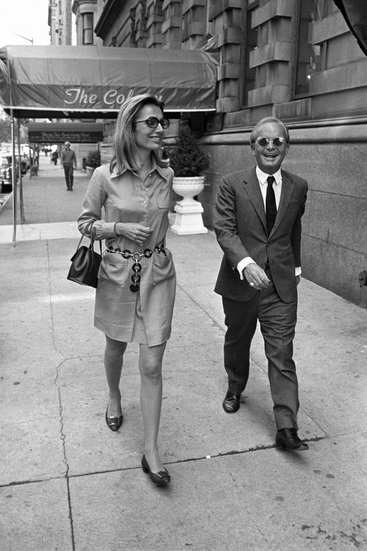 a man and woman walking down the sidewalk in front of a building on a city street