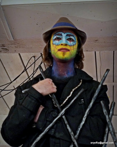 a man with his face painted in blue and yellow is holding two sticks up to his chest