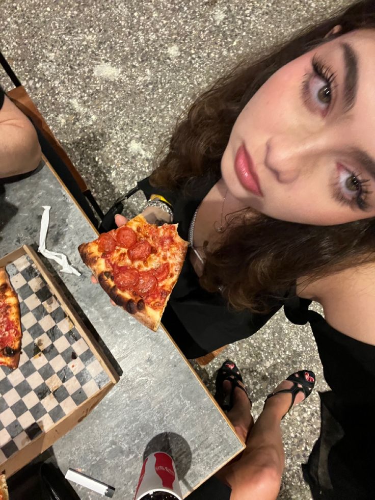 a woman sitting at a table with two slices of pizza in front of her,